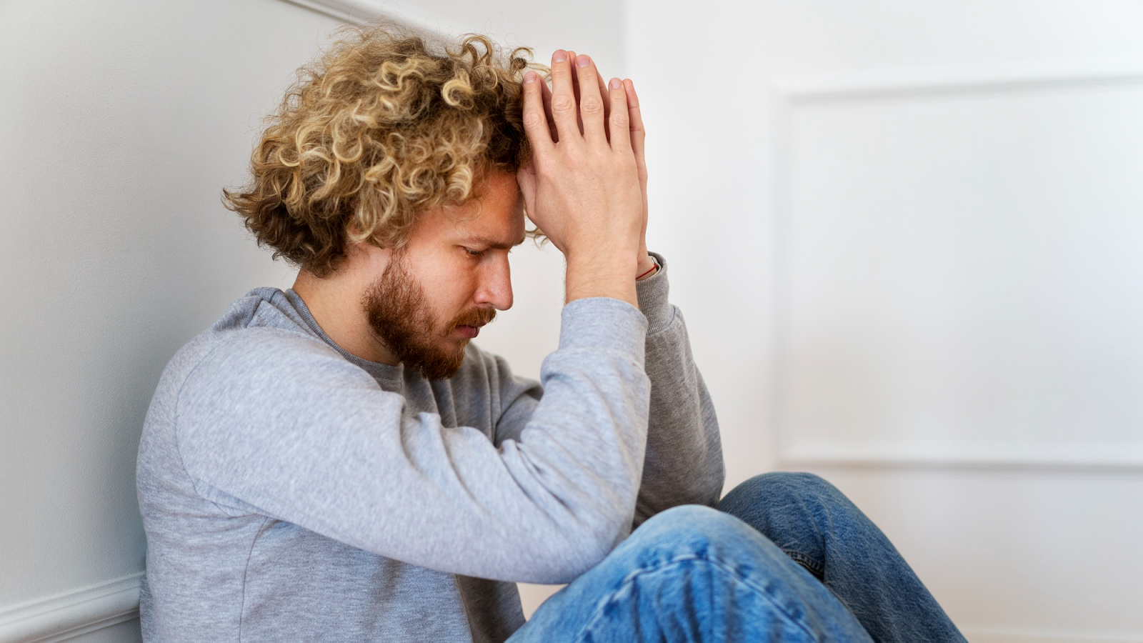 Mann, der auf dem Boden sitzt und die Hände über dem Kopf zusammenschlägt