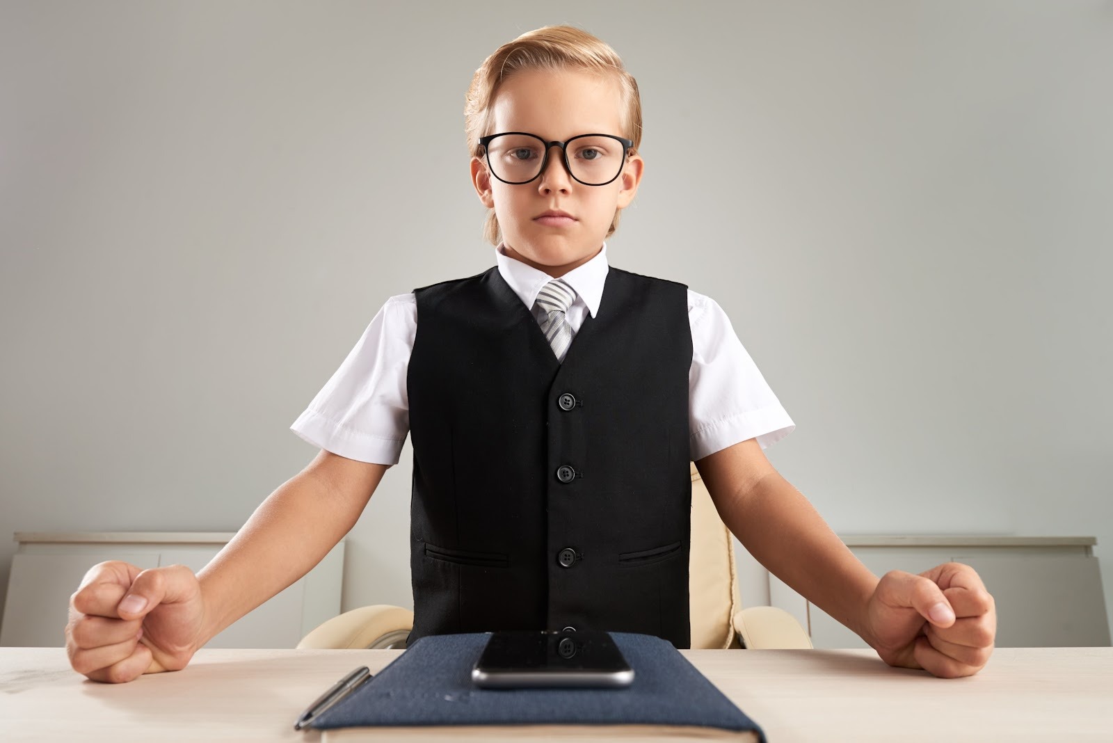 Ernst blickendes Kind in formeller Kleidung sitzt angespannt am Schreibtisch.