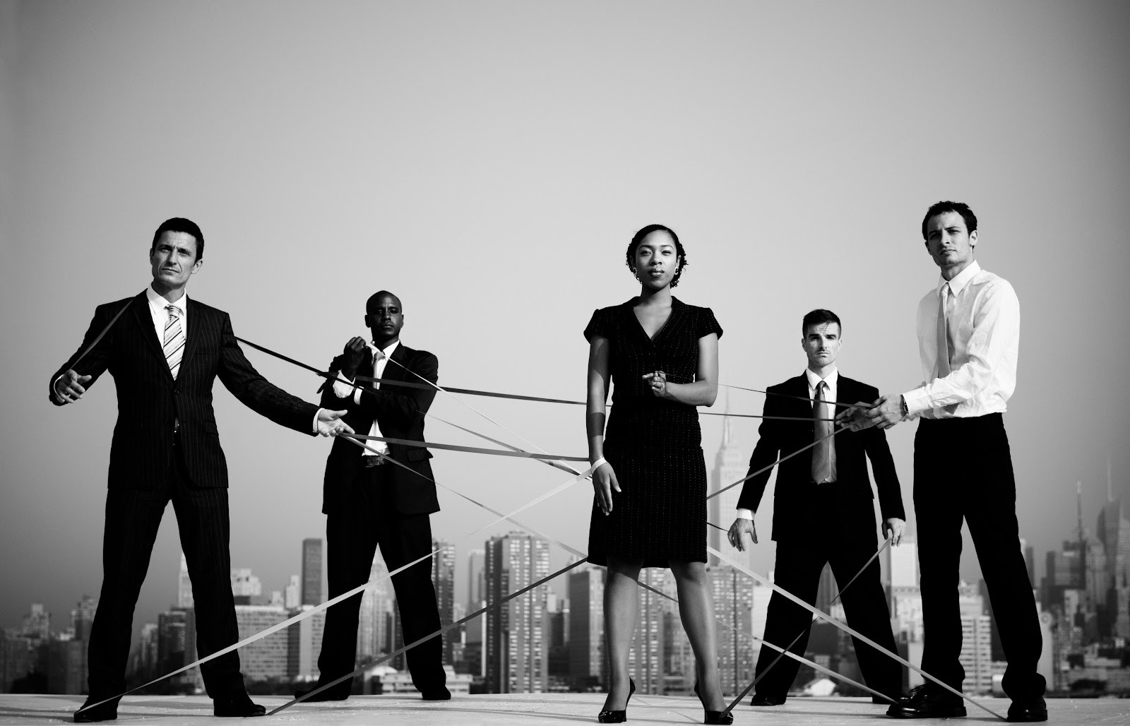Fünf Geschäftspersonen stehen vor einer Skyline und sind mit Bändern verbunden. 