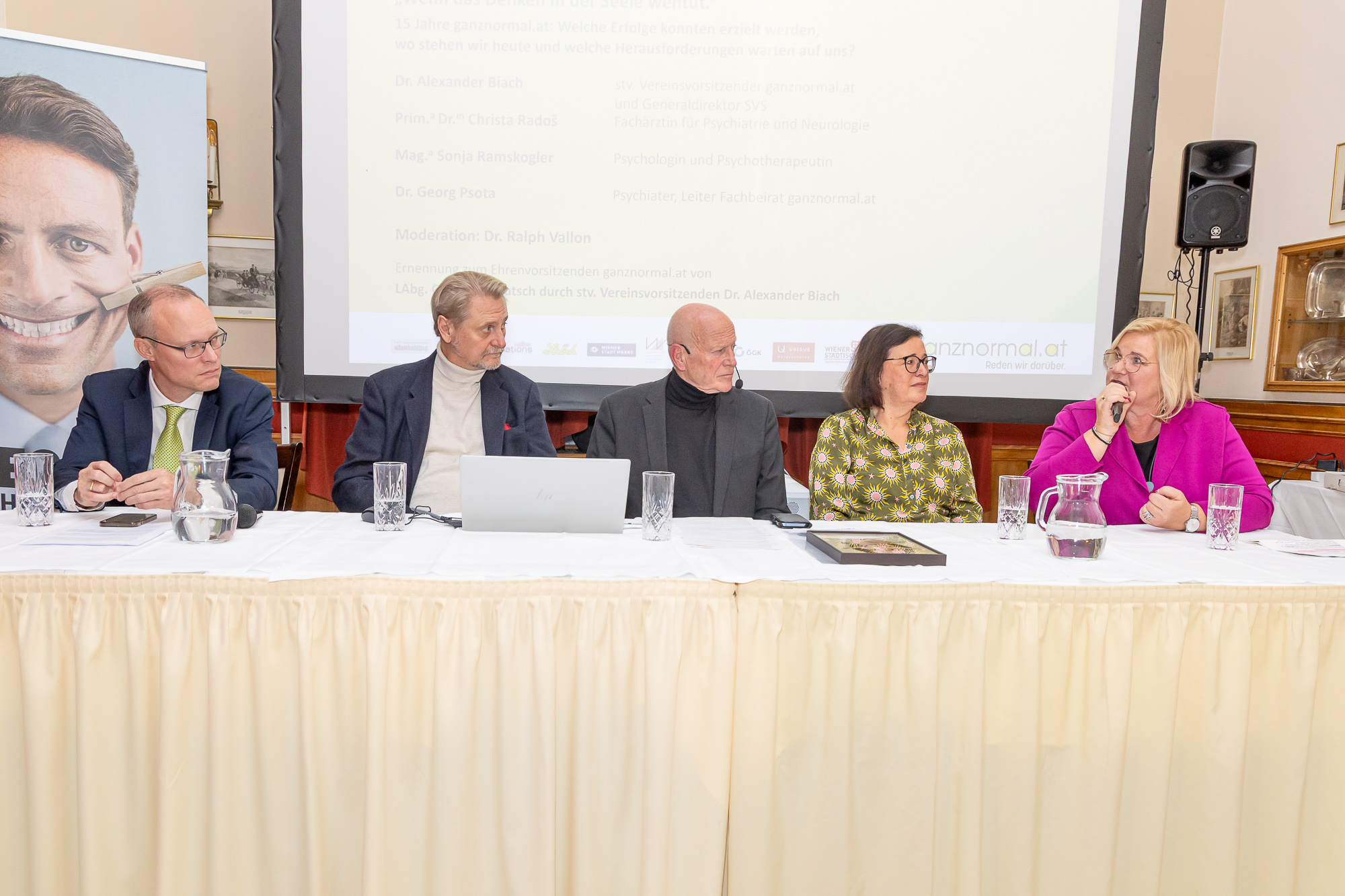 Fünf Teilnehmer diskutieren auf dem Podium der Jubiläumsveranstaltung von ganznormal.at. Eine Frau spricht in ein Mikrofon.