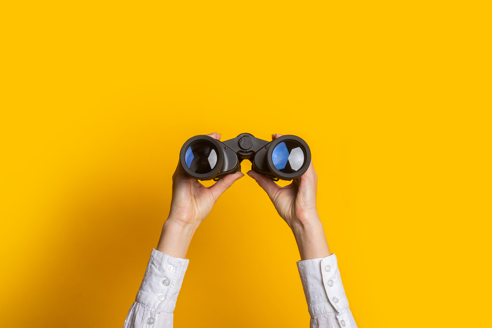 person holding binoculars up with yellow background