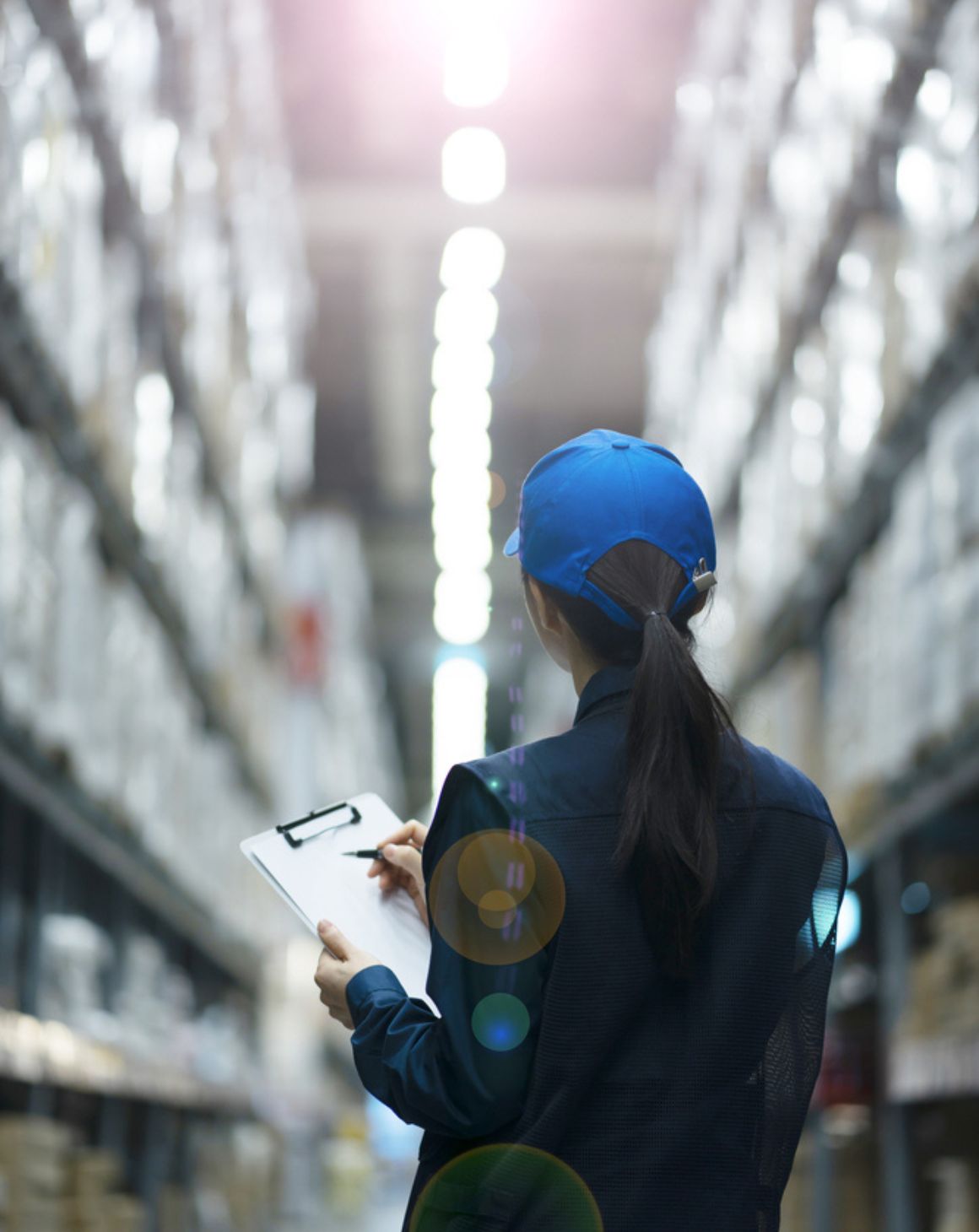 a woman stands in a warehouse, holding a clipboard and reviewing inventory amidst shelves of stored items
