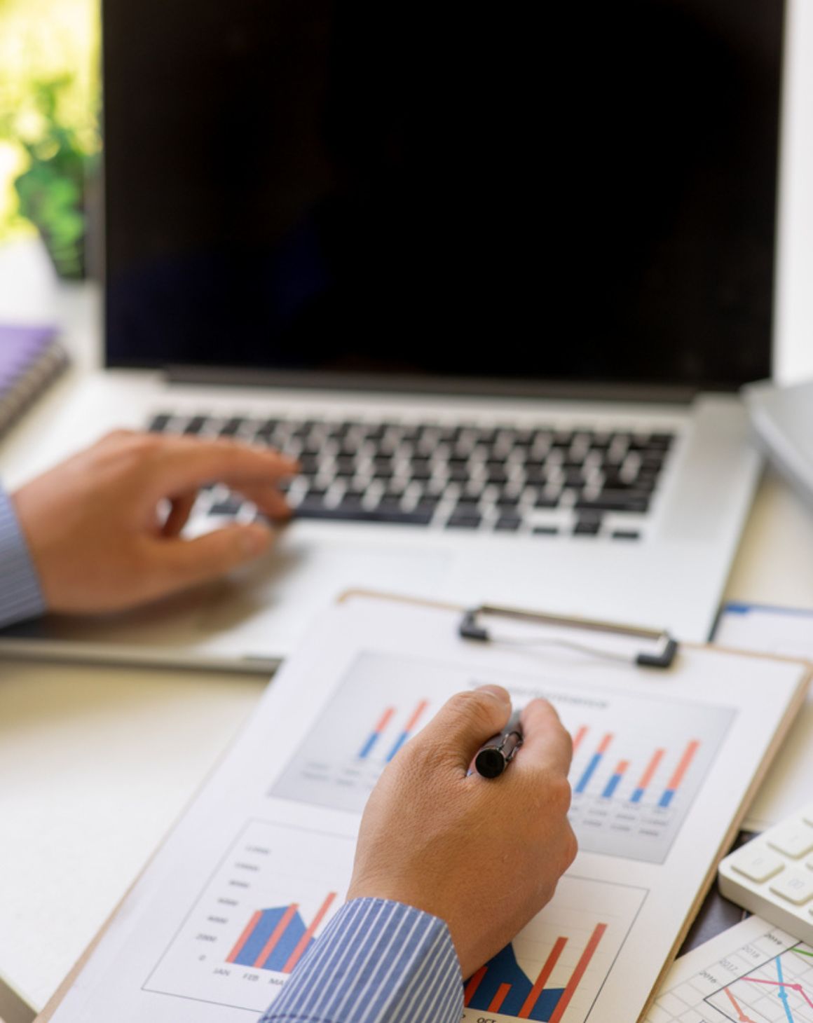 man at a desk with a laptop, writing on a report