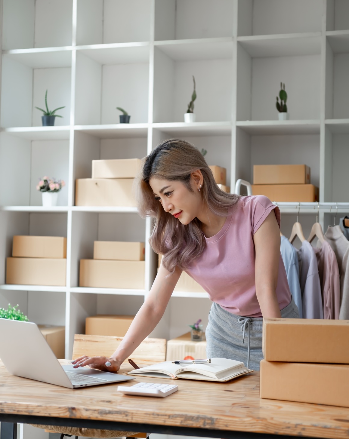 woman standing behind a desk with laptop, note book, and cardboard boxes