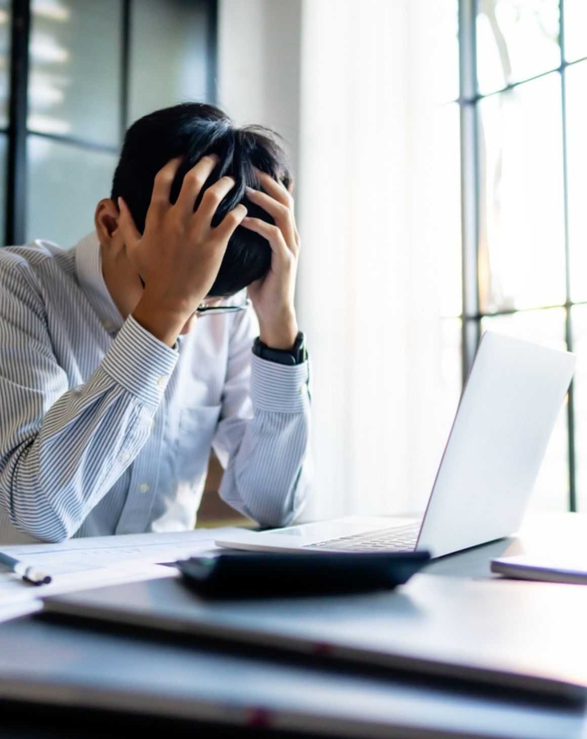 a man sits at a desk, resting his head in his hands, conveying a sense of frustration