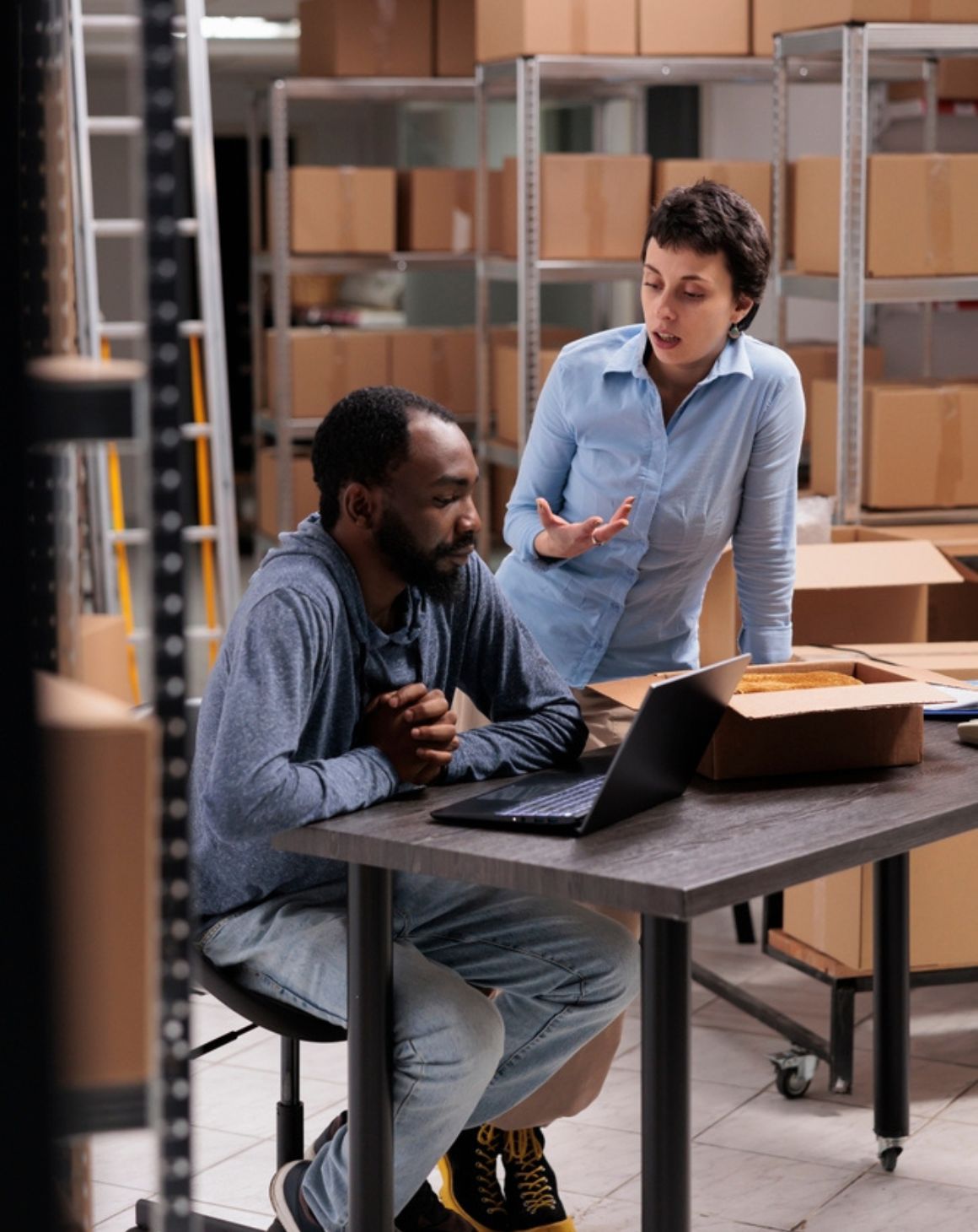 two individuals collaborating on tasks inside a warehouse, surrounded by shelves and boxes