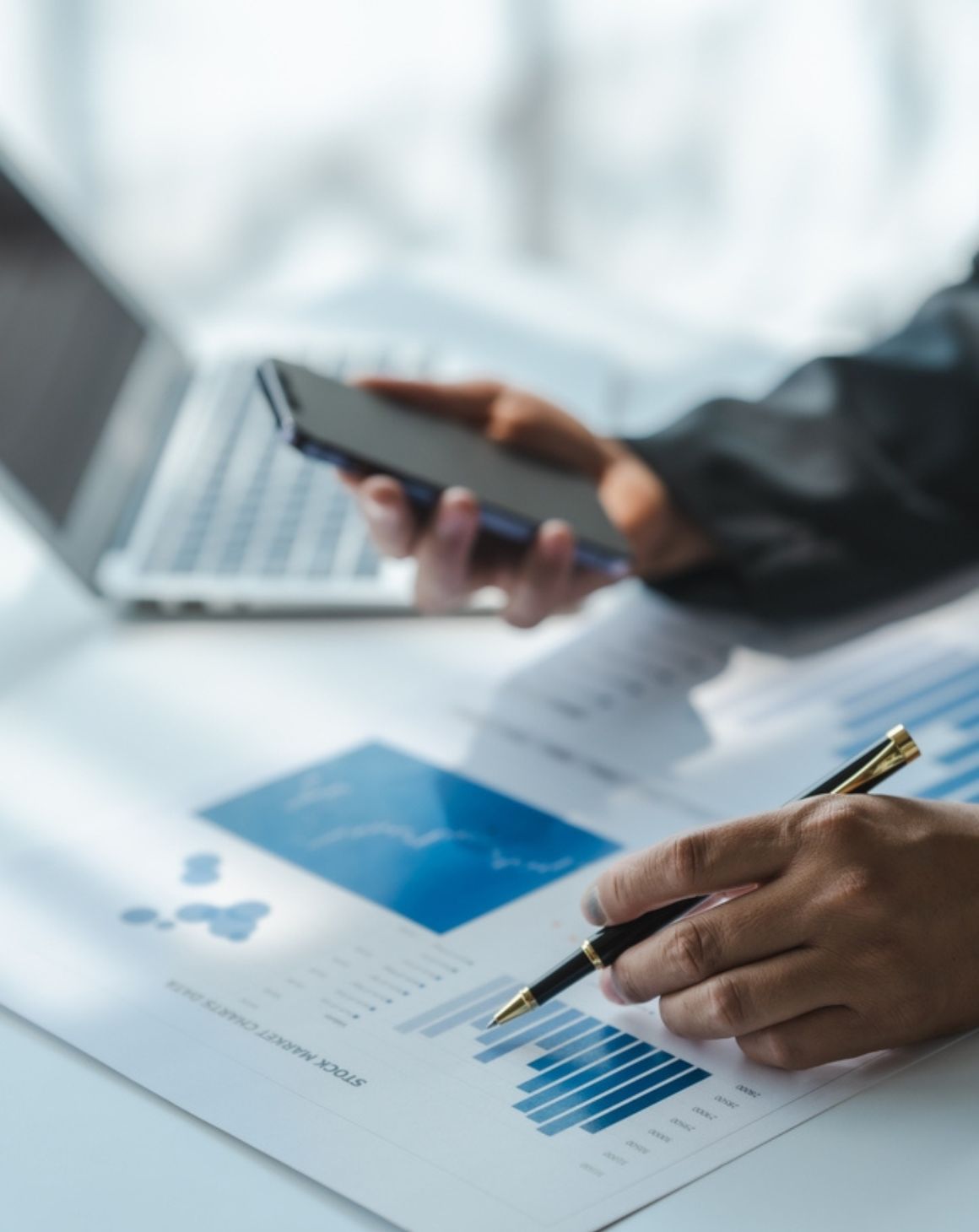 a businessman holding a pen over paper, with a laptop open beside him