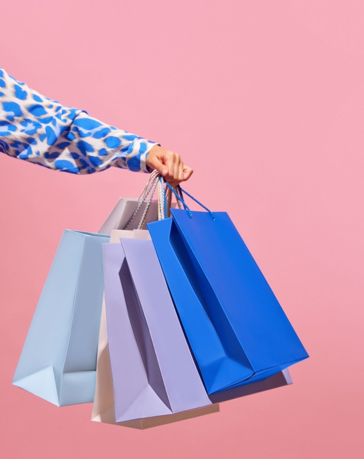 woman holding colorful shopping bags against a vibrant pink background