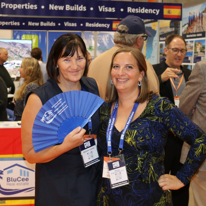 BluCee Real Estate owners Michelle and Henny posing with a hand fan in front of an exhibition stand