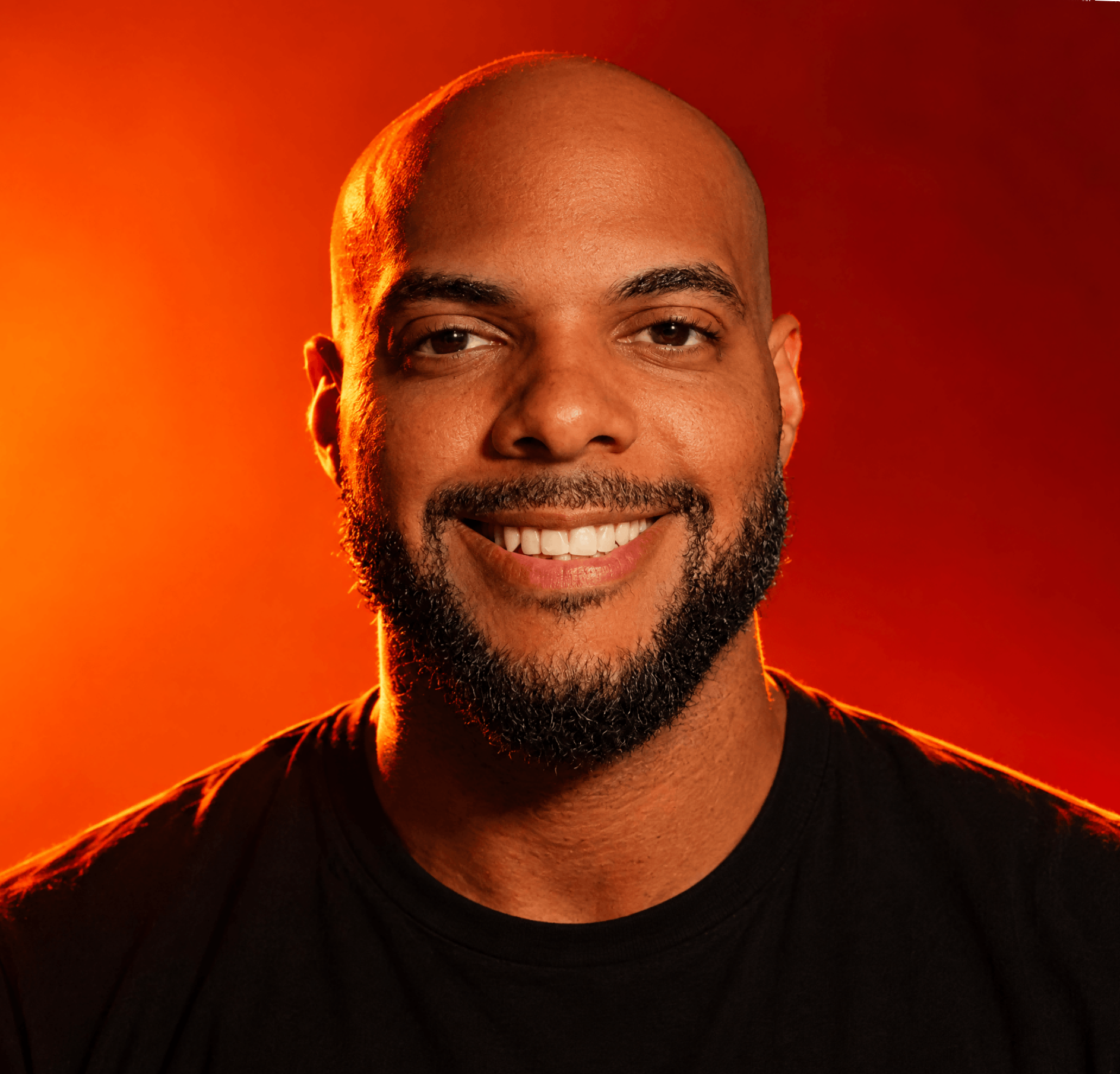 Portrait of a bald man with a beard wearing a black shirt against a dark background.