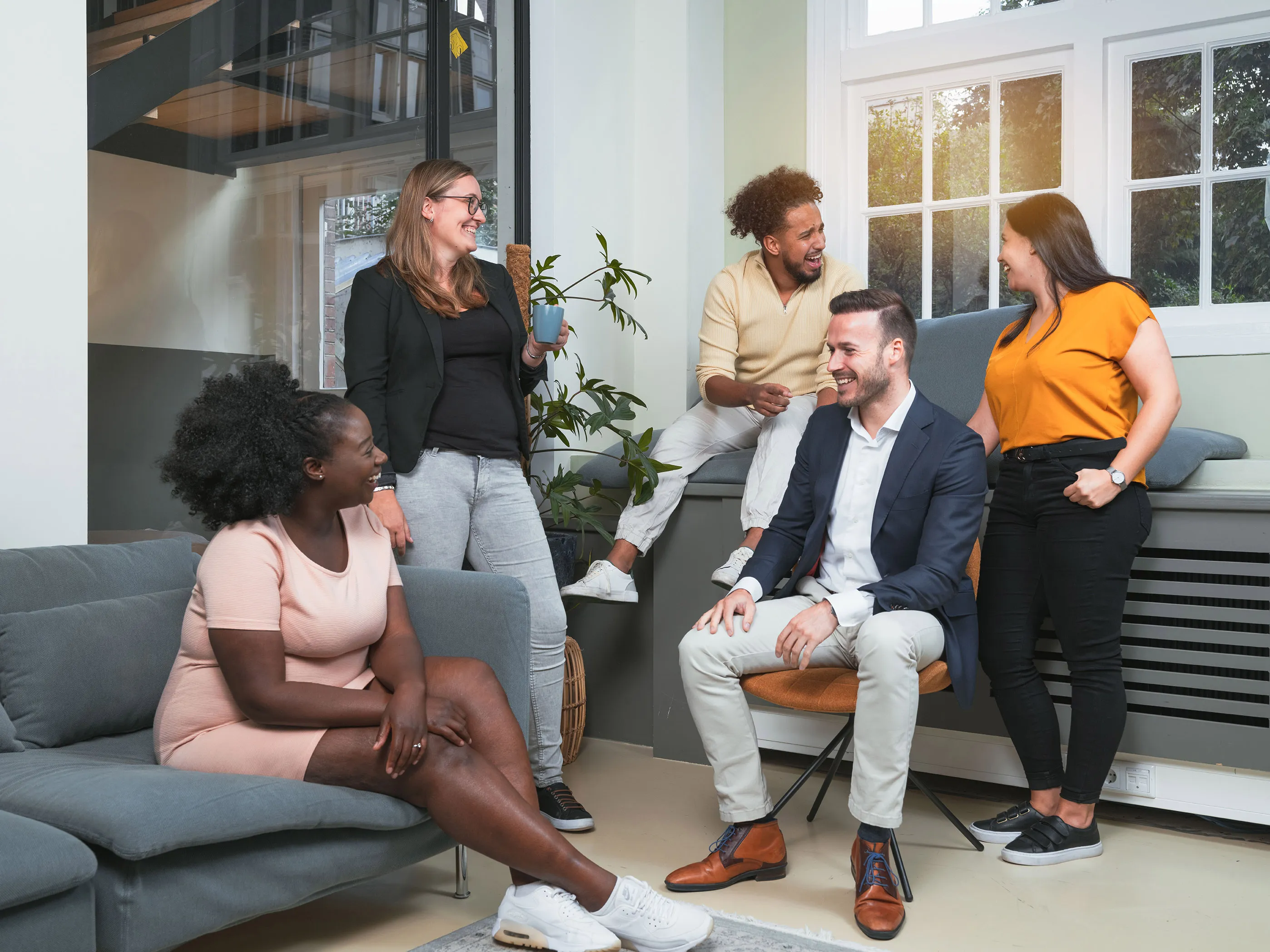 Group of five diverse young professionals smiling and chatting in a bright modern office lounge.