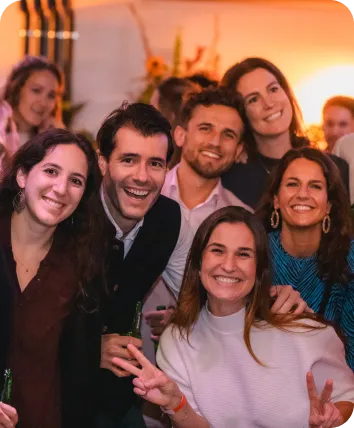 Group of six smiling friends posing for a photo at a lively indoor party.