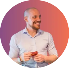 Smiling man with short hair and beard holding a red card, against a circular purple to orange gradient background.