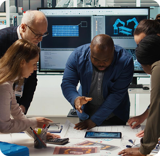 Four professionals collaborating over architectural plans and digital devices in an office with screens displaying 3D design models in the background.