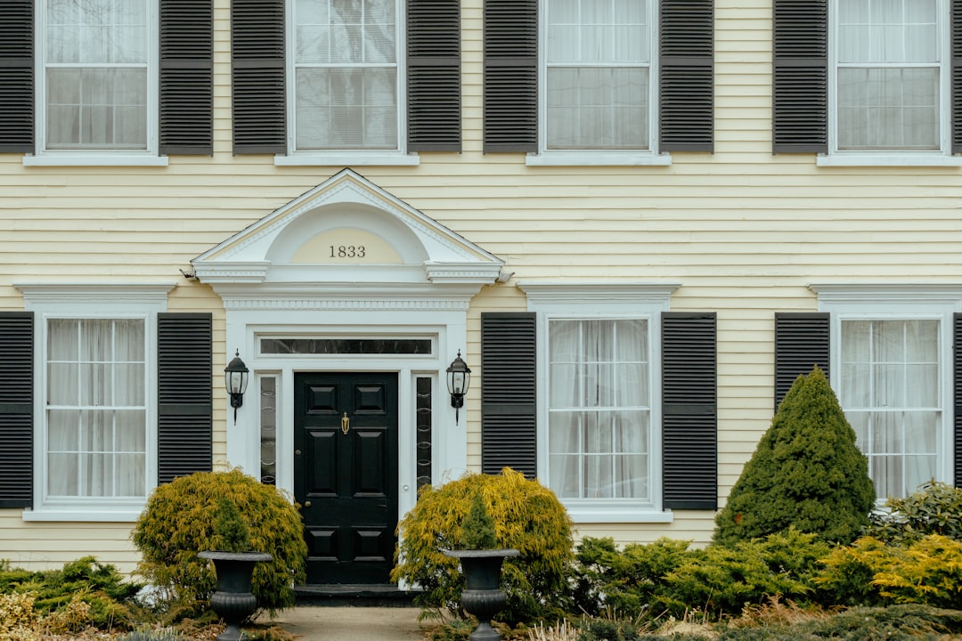 Historic yellow house with black shutters, 1833 entrance, potted plants