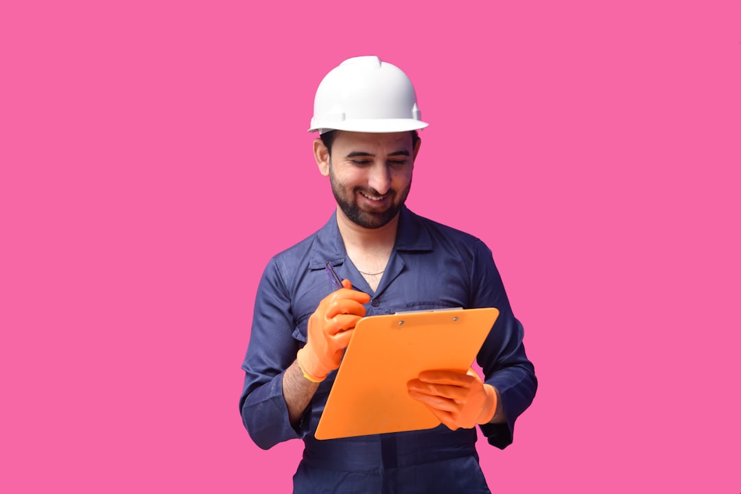 Construction worker in white helmet takes notes on orange clipboard