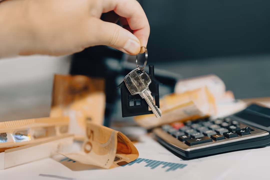 hand with home key above table and calculator and money - homeowners insurance calculator massachusetts concept