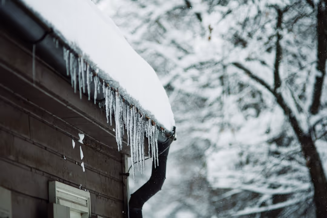 A snow-covered roof with icicles hanging from the gutters in a residential Massachusetts neighborhood - homeowners insurance worcester ma