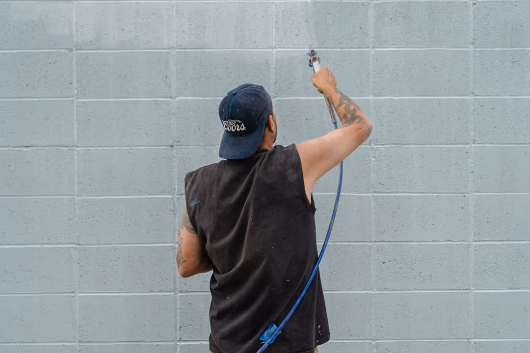painter using a paint sprayer on an exterior wall - liability insurance for painting company