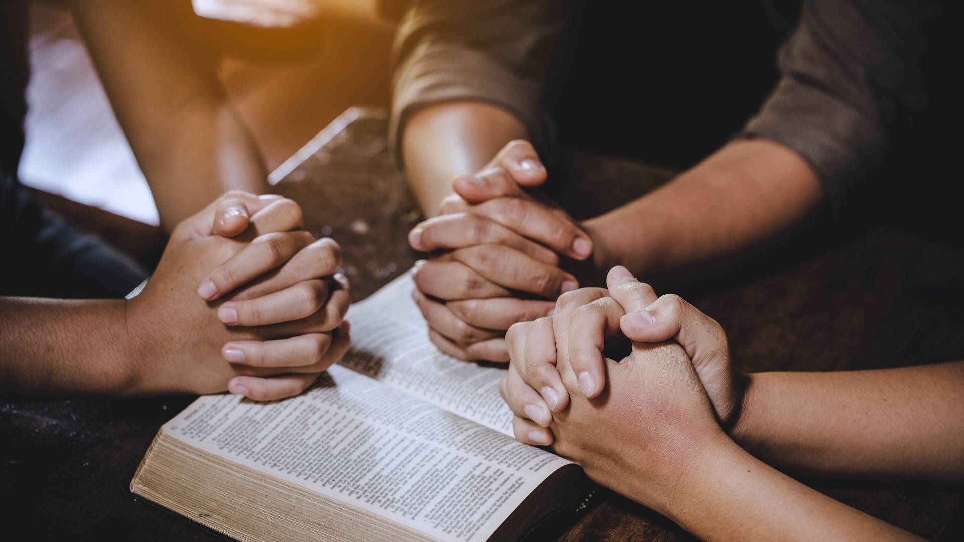 Three hands folded on Bible