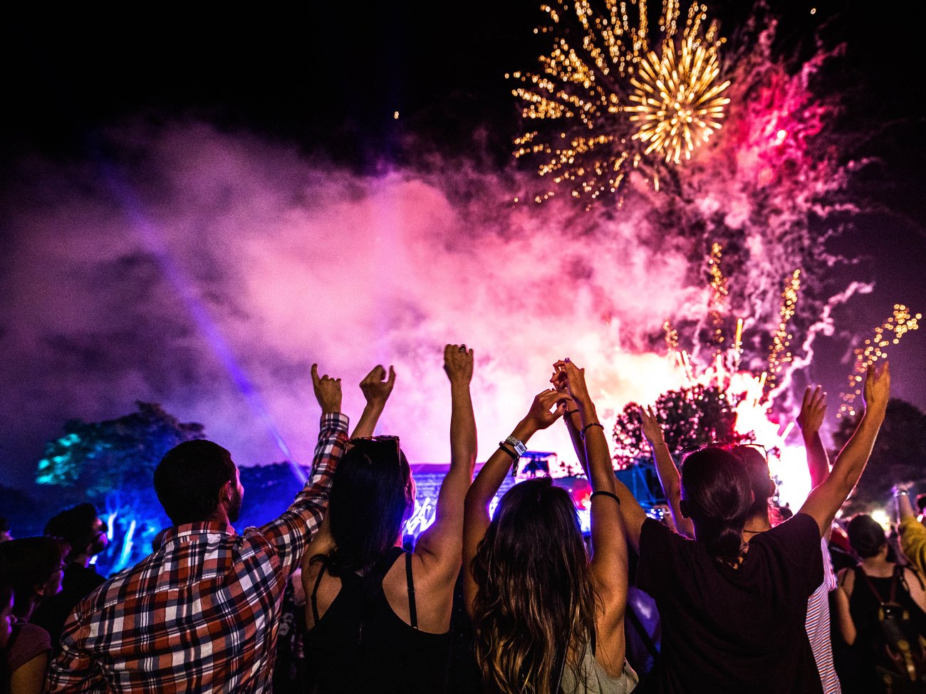 Festival crowd with hands in the air beneath fireworks