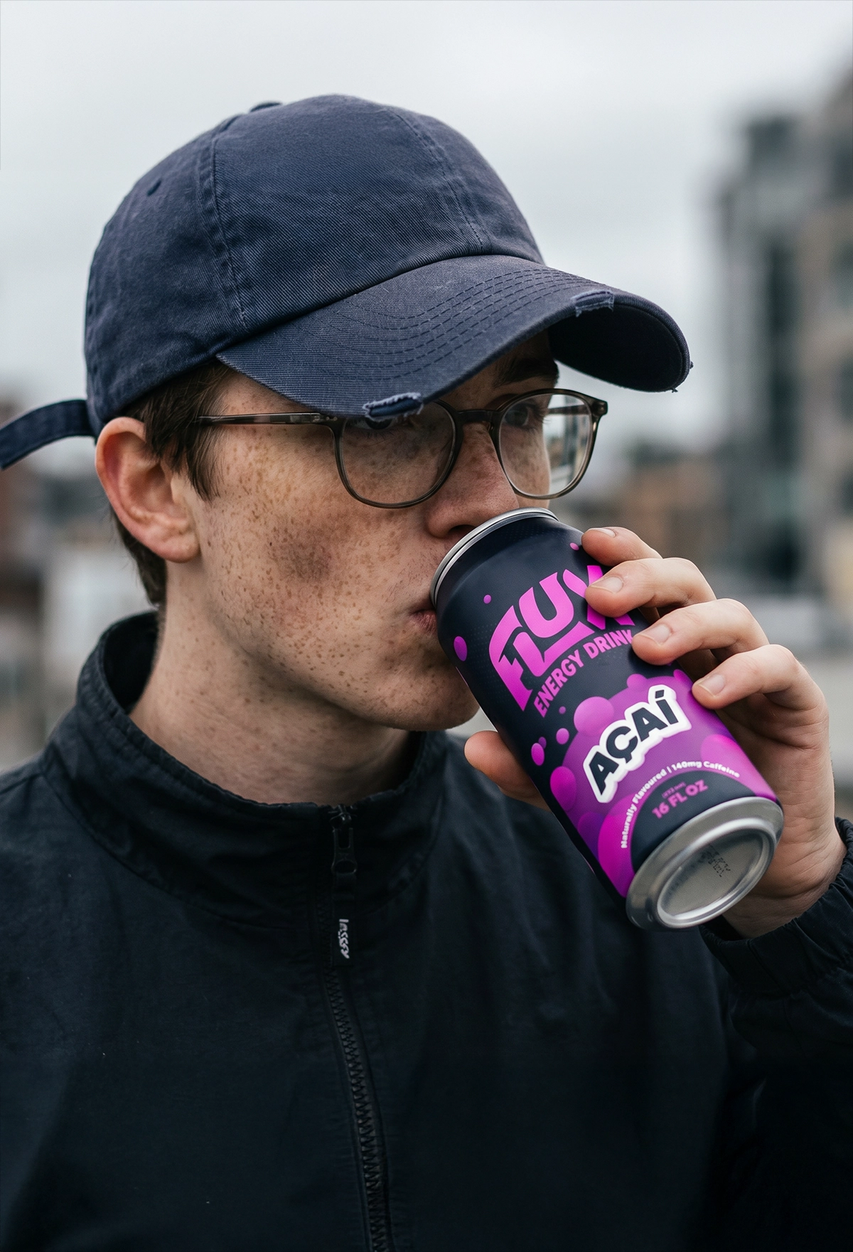 Image of a guy outside with a baseball cap on, drinking from a Flux energy drink can.