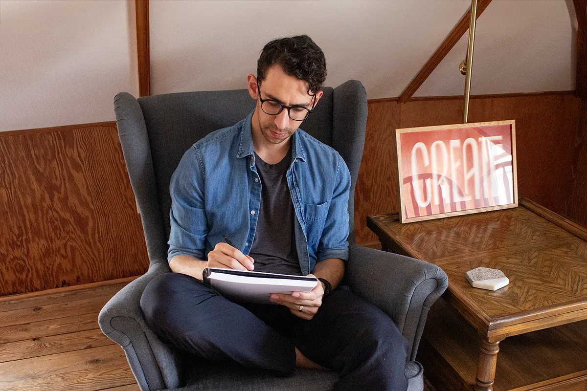 Picture of Jeremy sitting in an armchair sketching in his sketchbook.