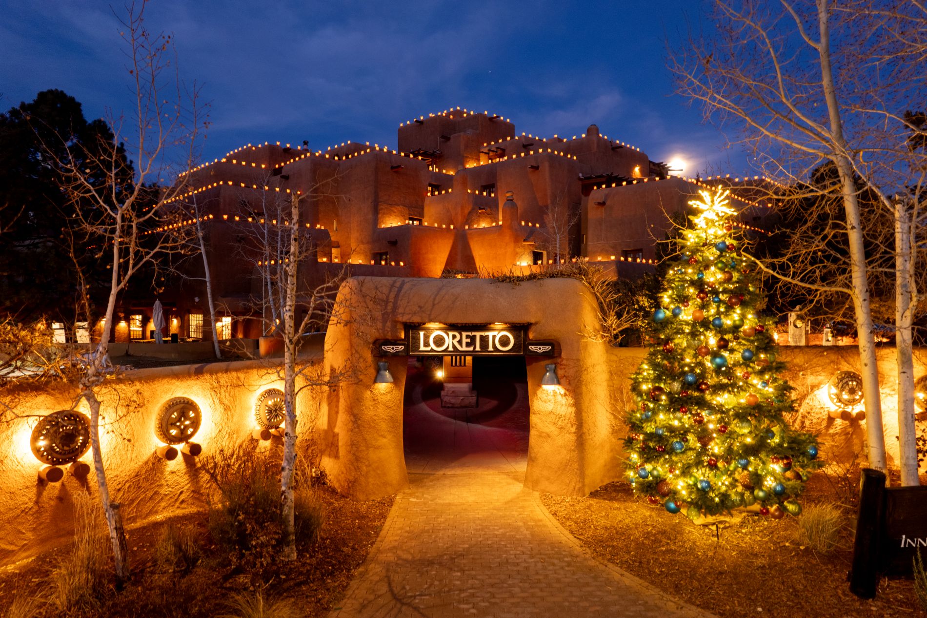 Exterior image of Loretto at night with Christmas tree in front and luminarias lining the roor