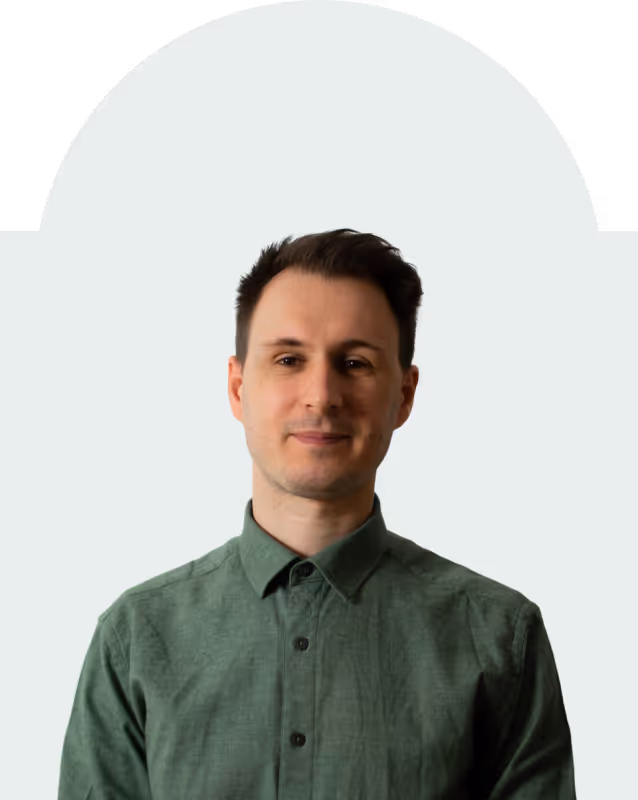 Man with short dark hair wearing a green button-up shirt against a light gray background.