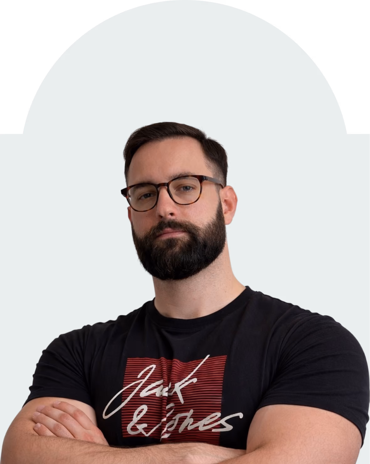 Bearded man wearing glasses and a black t-shirt with a red and white graphic, arms crossed.