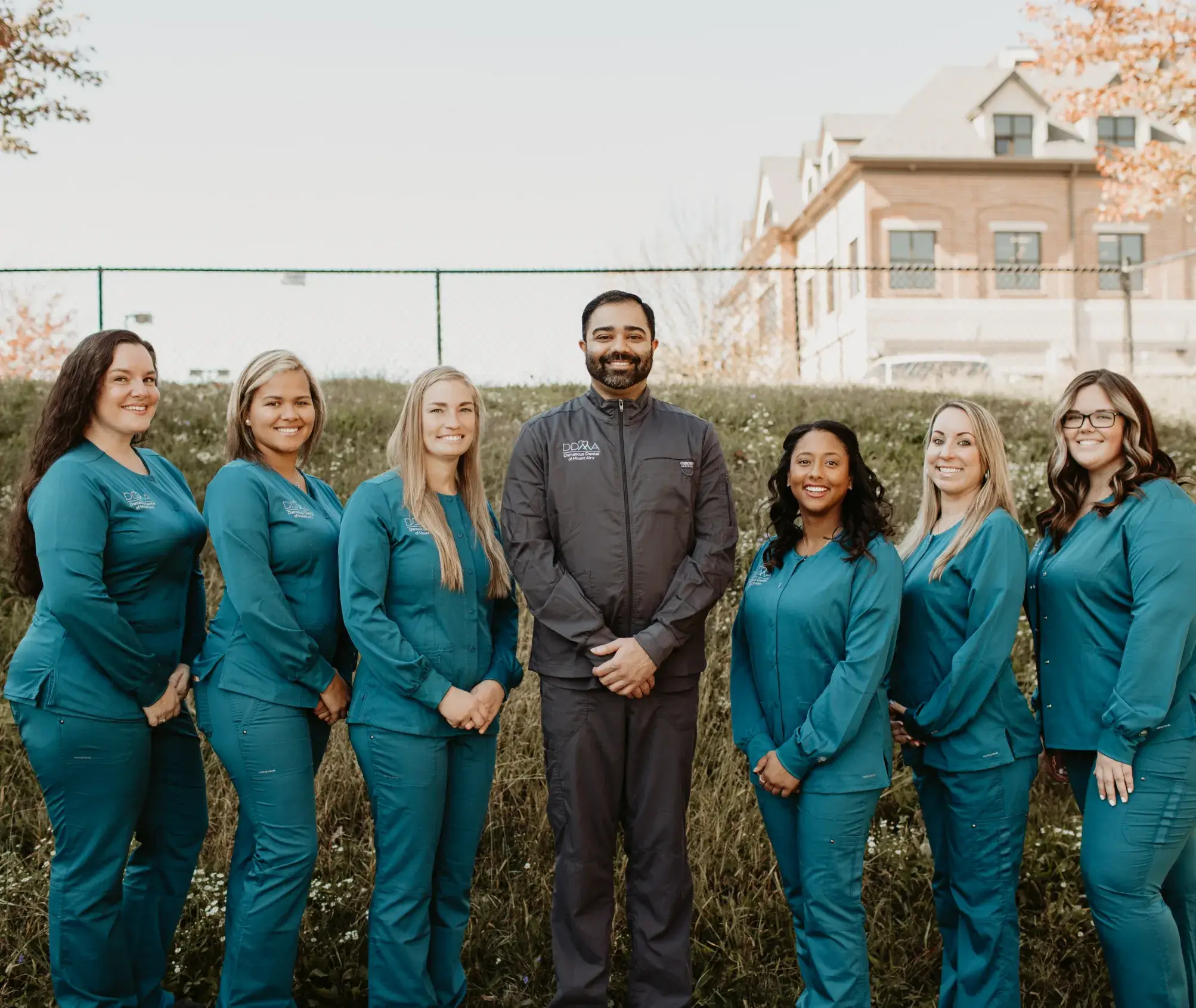 A group of women in scrubs standing in front of a fence.