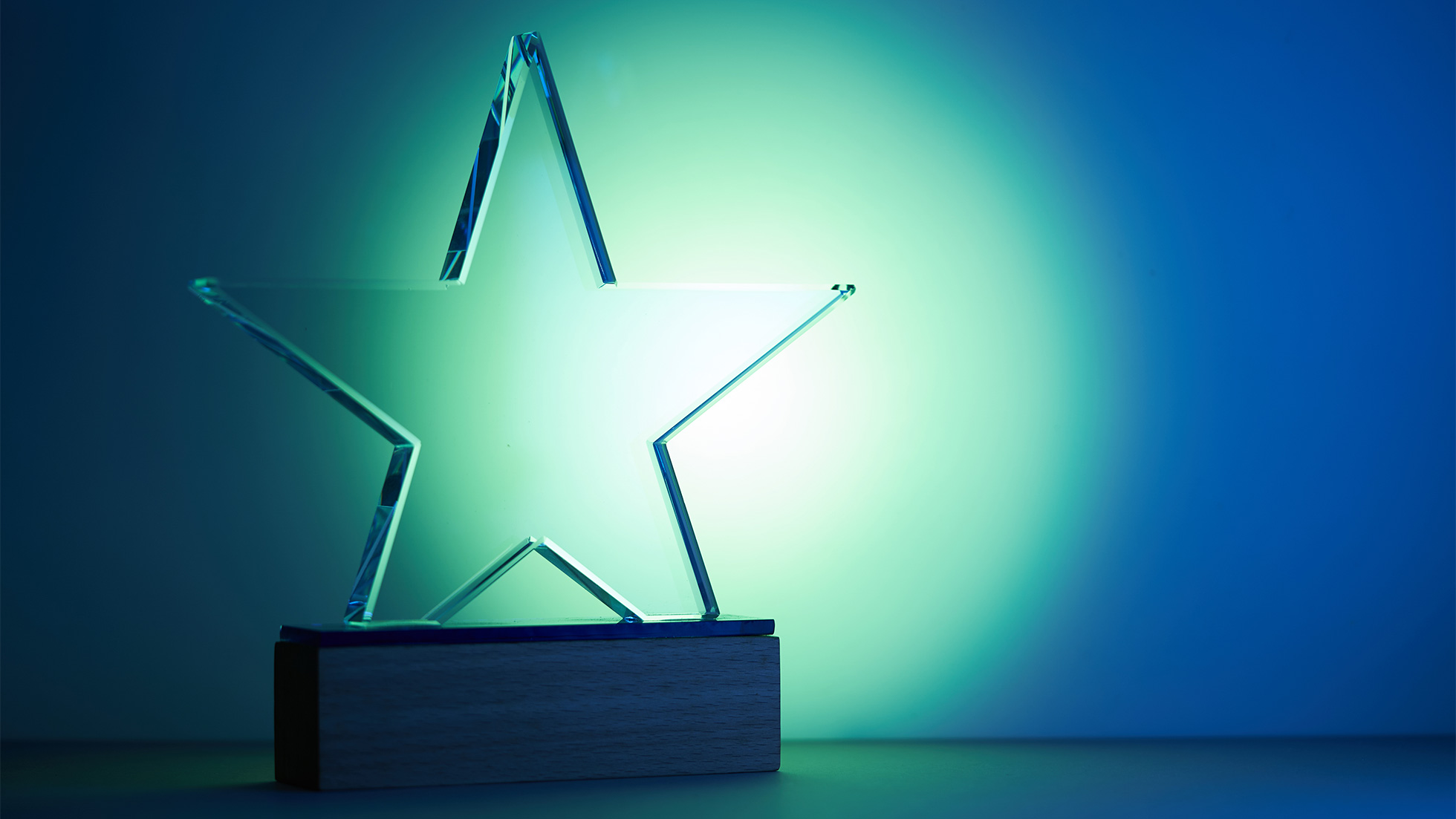 A crystal star award sitting against a blue background with a bright spotlight shining on it.