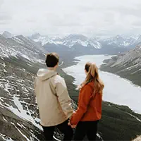 Couple overlooks snowy mountain valley hand in hand