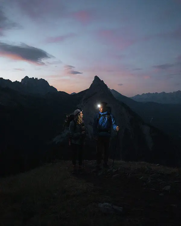 Couple hiking on mountain summit with headlamps during blue hour light