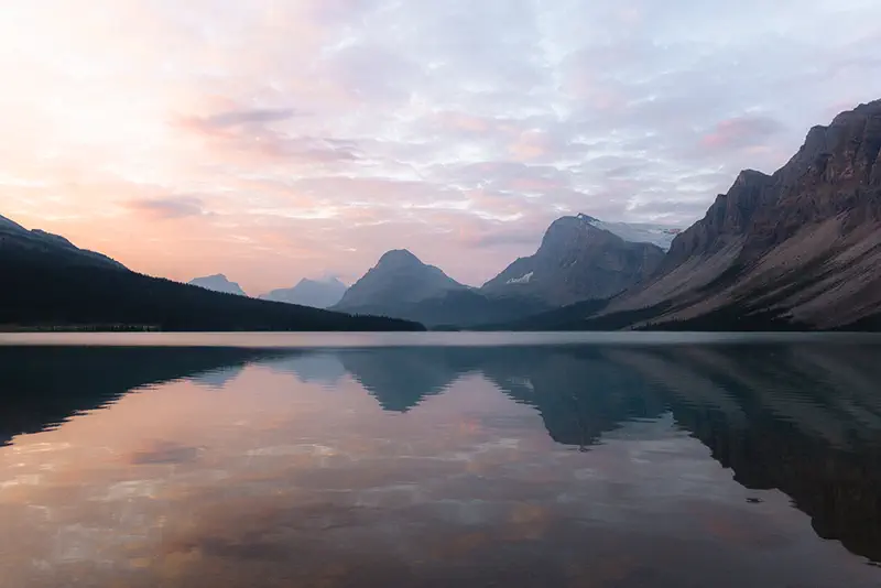 Perfect mirror reflection of Rocky Mountain peaks in Bow Lake during soft sunrise light