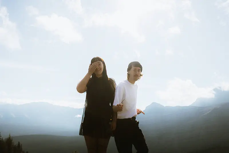 Man strikes playful pose while girlfriend laughs during mountain adventure session in Banff