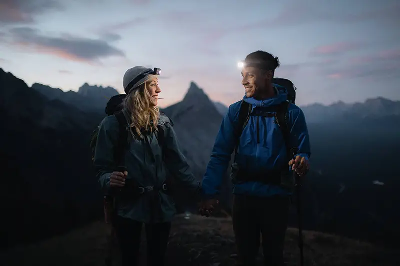 Laughing couple shares intimate moment on mountain summit with headlamps during blue hour light