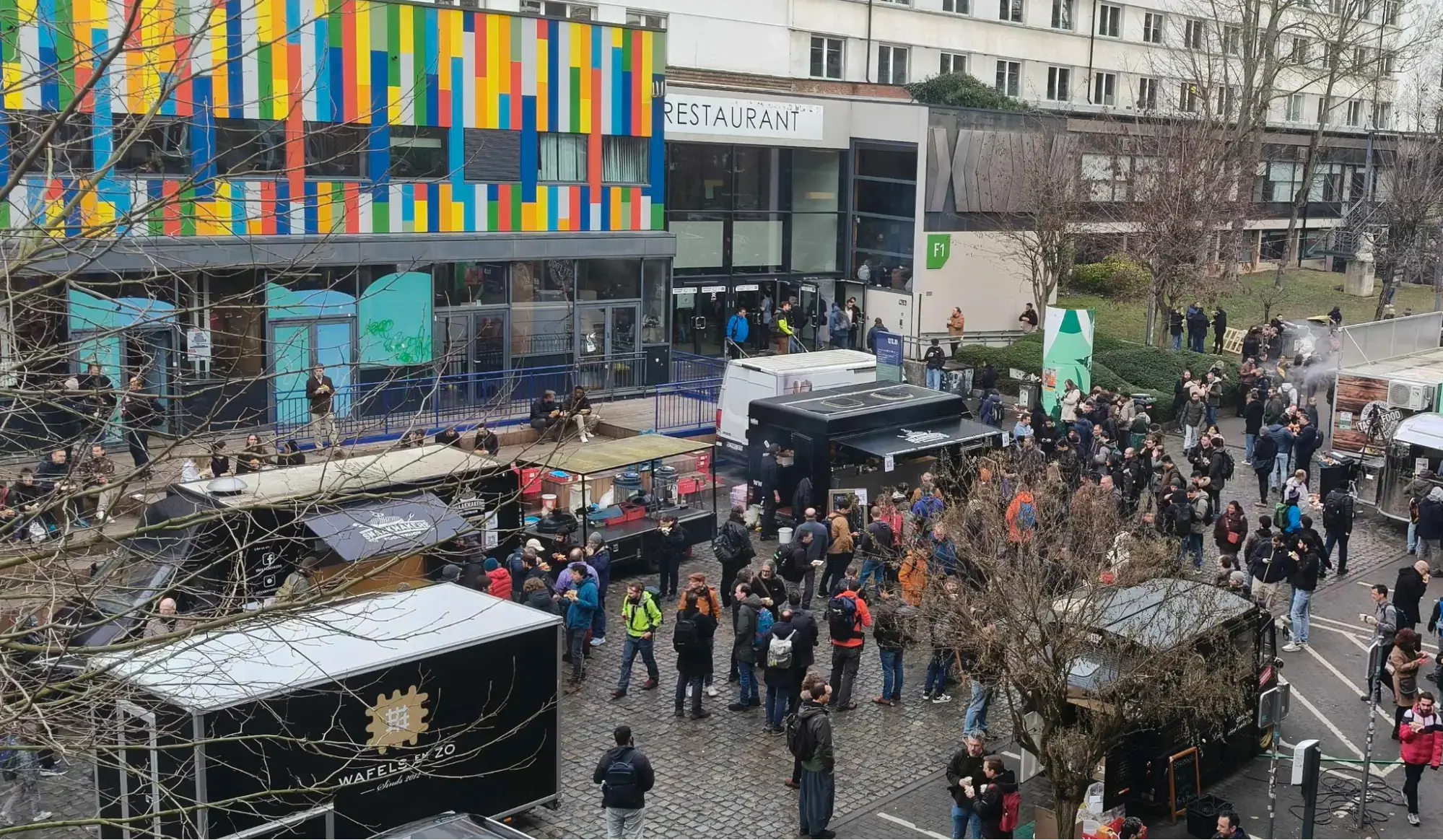 Lunchtime at FOSDEM, people hurrying out of the lecture rooms towards a street full of food trucks.