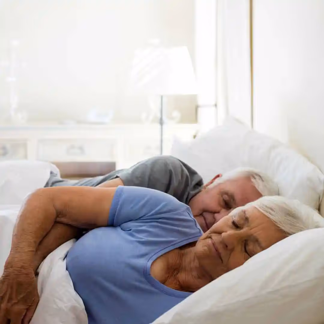An elderly couple sleeping in bed.