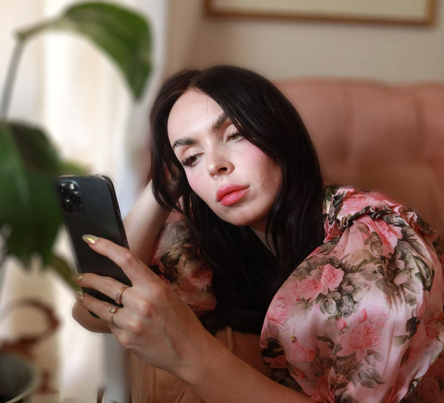 An attractive woman wearing a floral dress, reclining on a sofa looking at her phone
