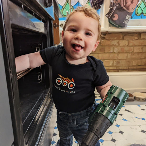 Smiling technician in navy shirt fixing a modern built-in oven with a screwdriver in a kitchen.