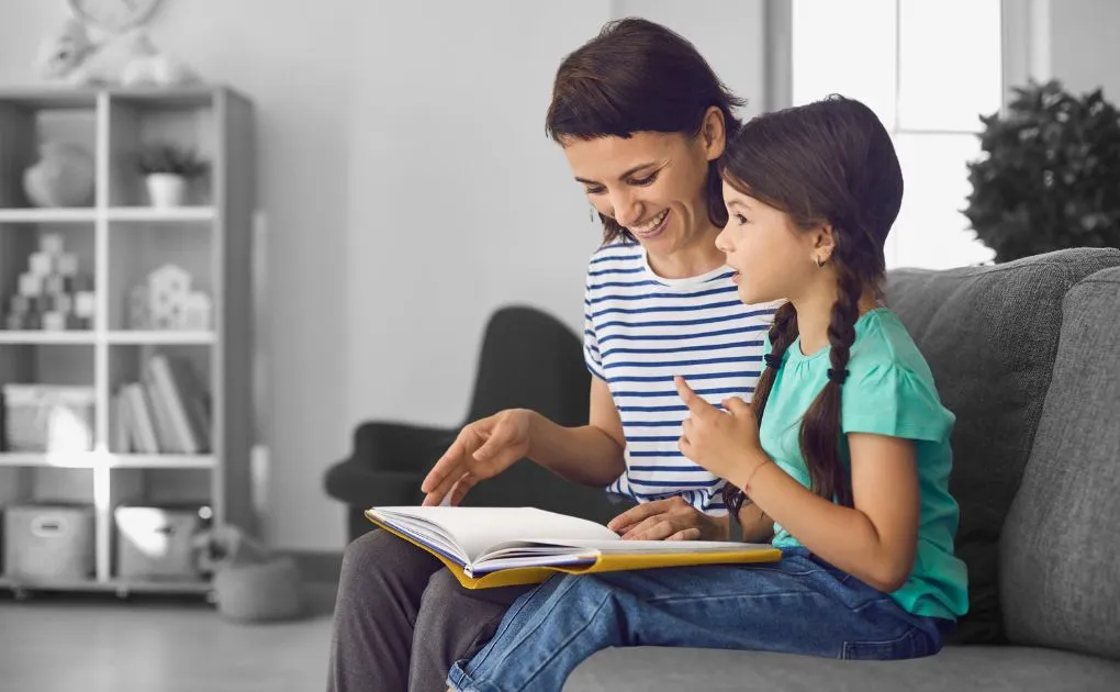 A woman and a little girl sitting on a couch looking at a book.