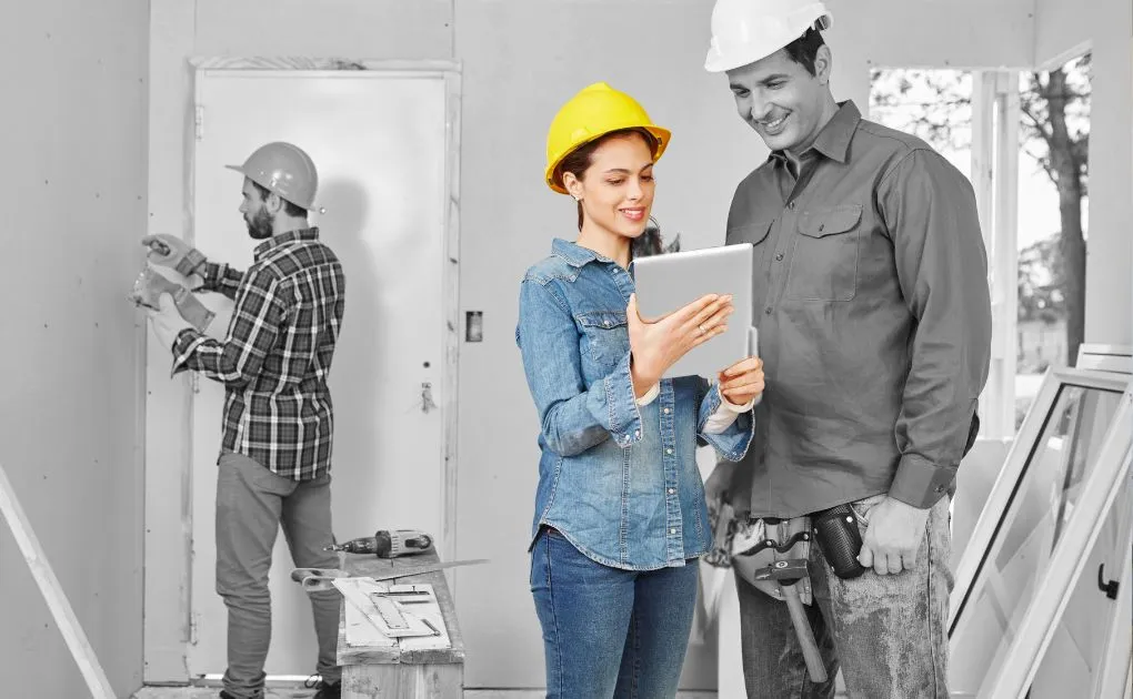 A man and a woman in hardhats looking at a tablet.