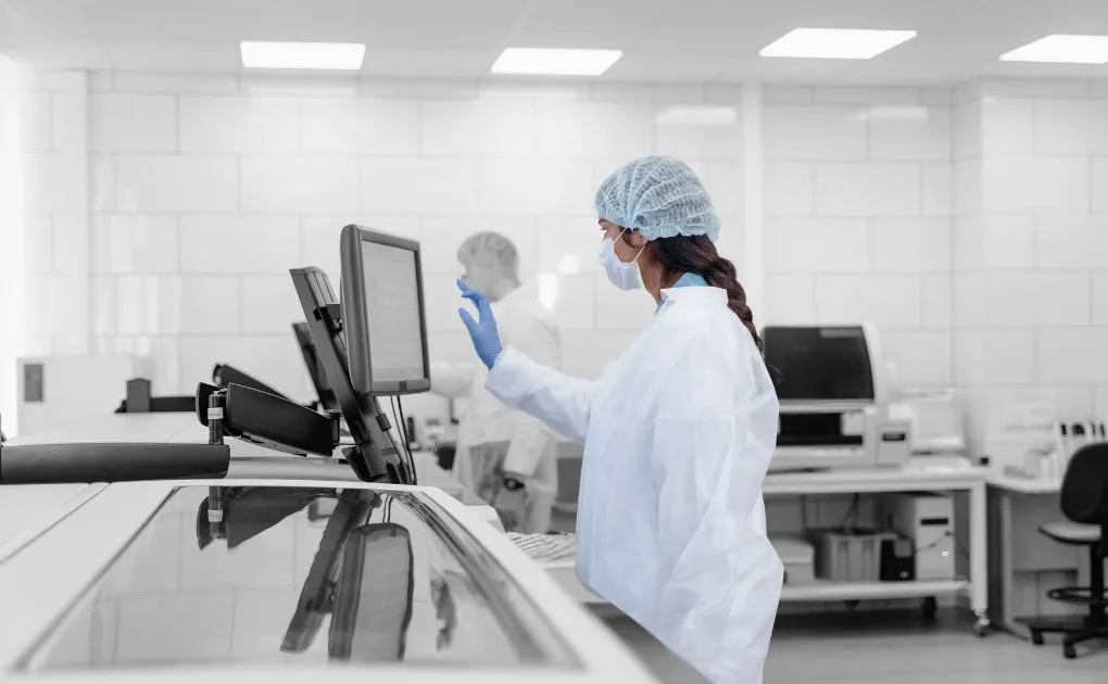 A woman in a white lab coat working on a computer.