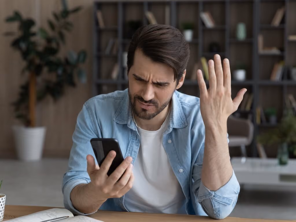 A millennial male with a frustrated expression, staring at his mobile phone.