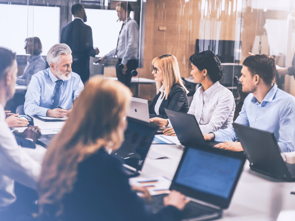 A group of people sitting at a conference table with laptops