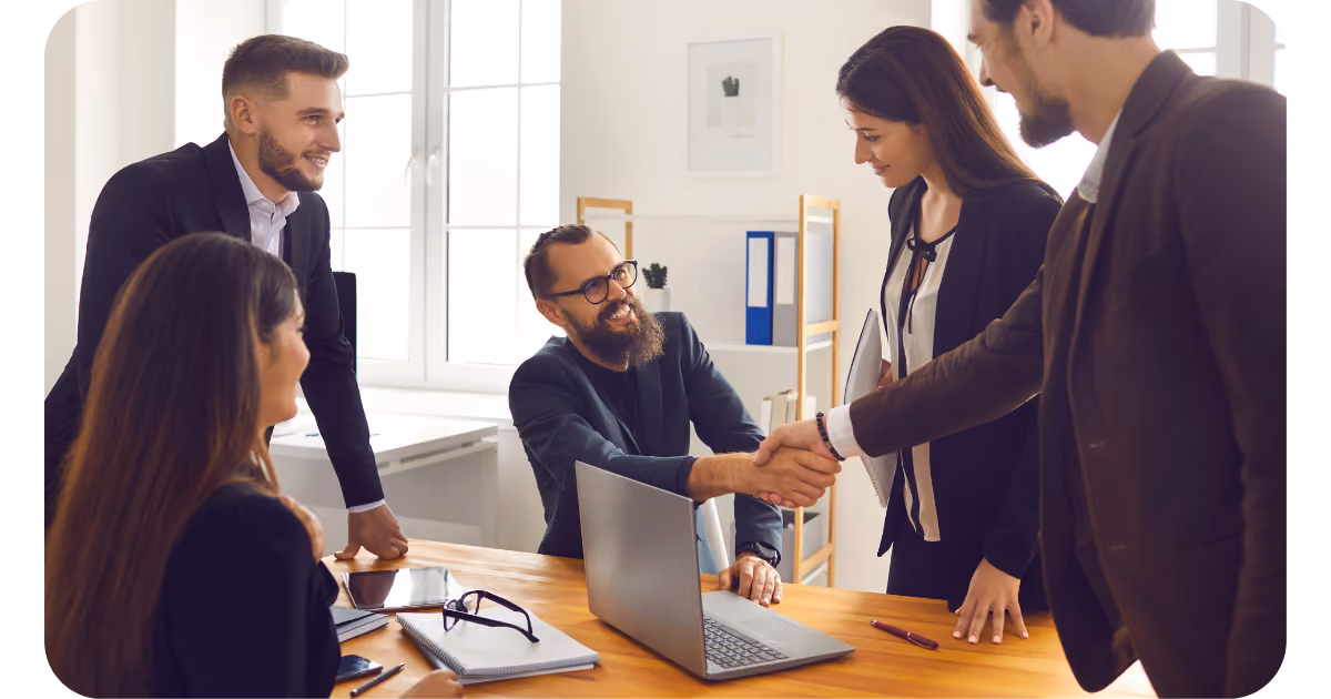 A group of business people shaking hands in front of a laptop