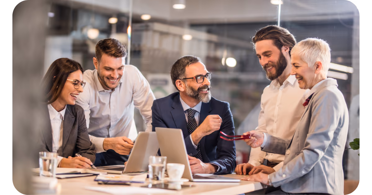 a group of business people sitting around a table looking at a laptop