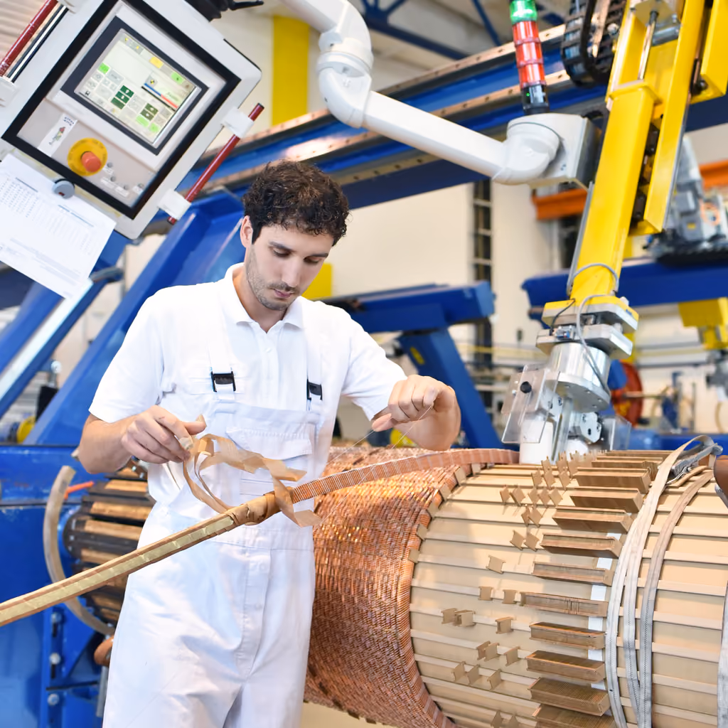 Young mechanical engineering workers operate a machine for winding copper wire - manufacture of transformers in a factory
