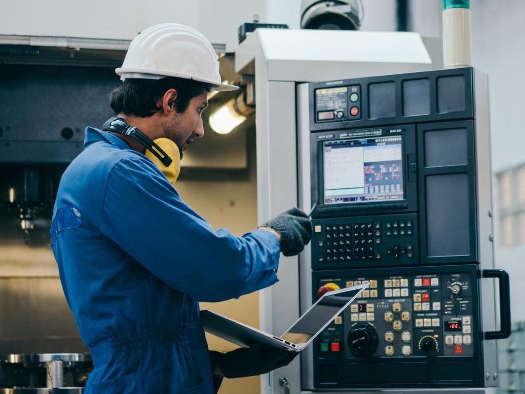 male factory orker using a laptop to programme a machine